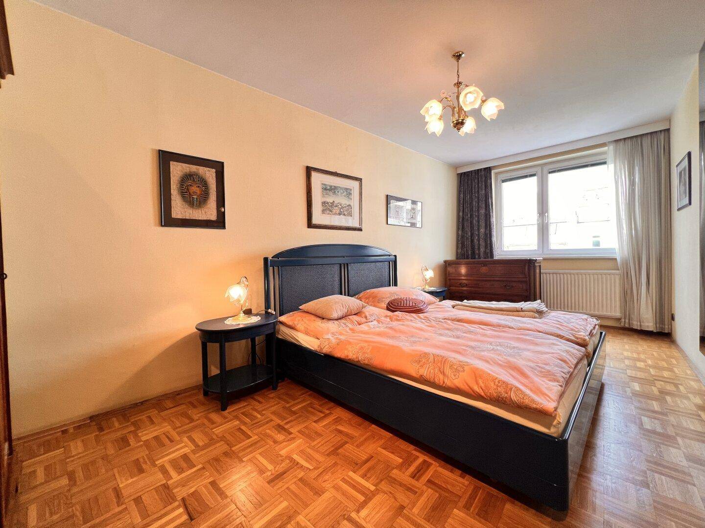 Gemütliches Schlafzimmer mit Doppelbett, Nachttischen und Parkettboden, gut beleuchtet durch ein Fenster.