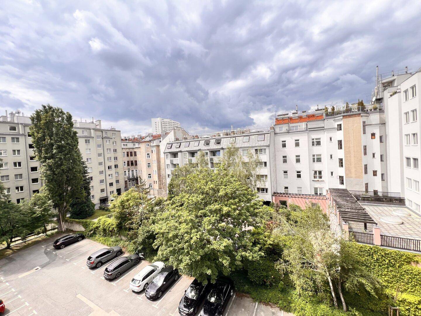 Außenansicht eines Wohnkomplexes mit Parkplätzen und viel Grünfläche unter bewölktem Himmel.