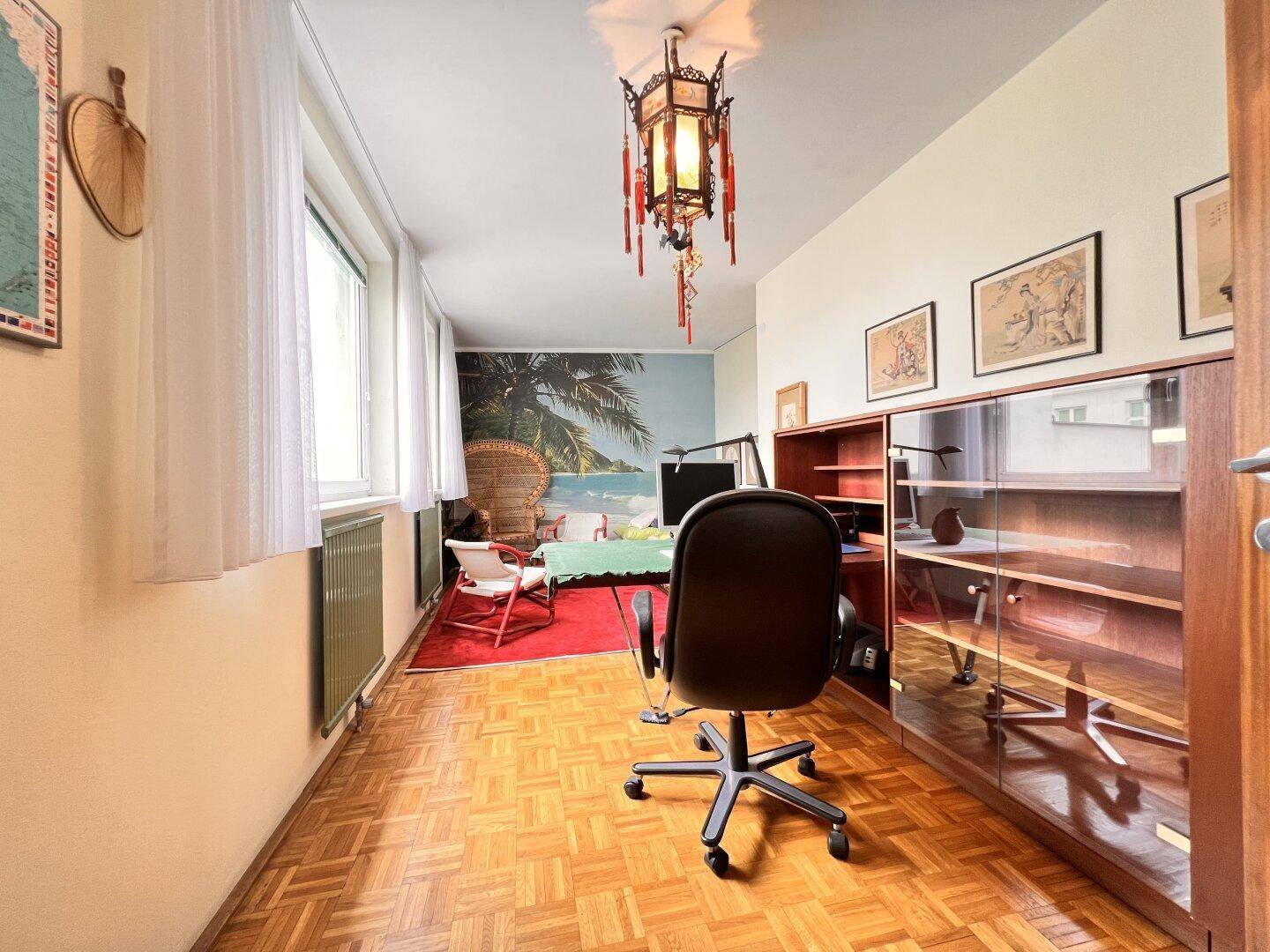 Arbeitszimmer mit Schreibtisch, Bücherregal und einer auffälligen Wandtapete mit Strandmotiv.