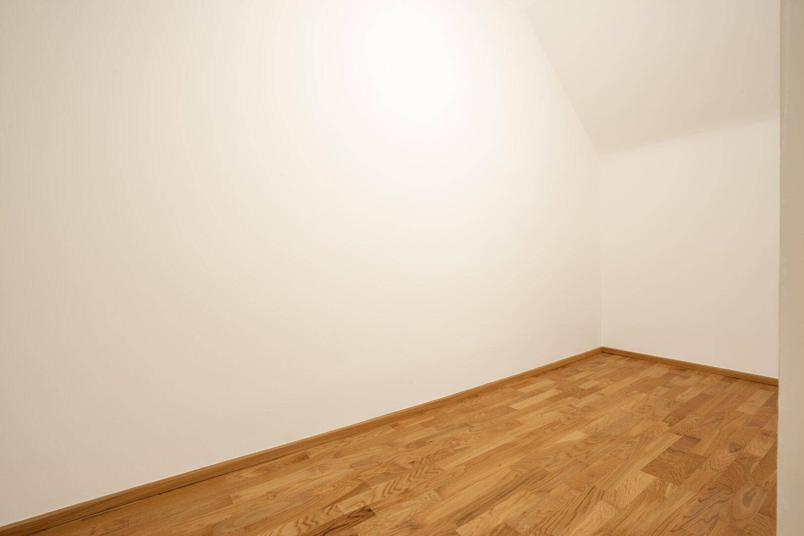 Leerer Raum mit Parkettboden und Dachschräge, ideal als Abstellraum oder kleines Zimmer nutzbar.