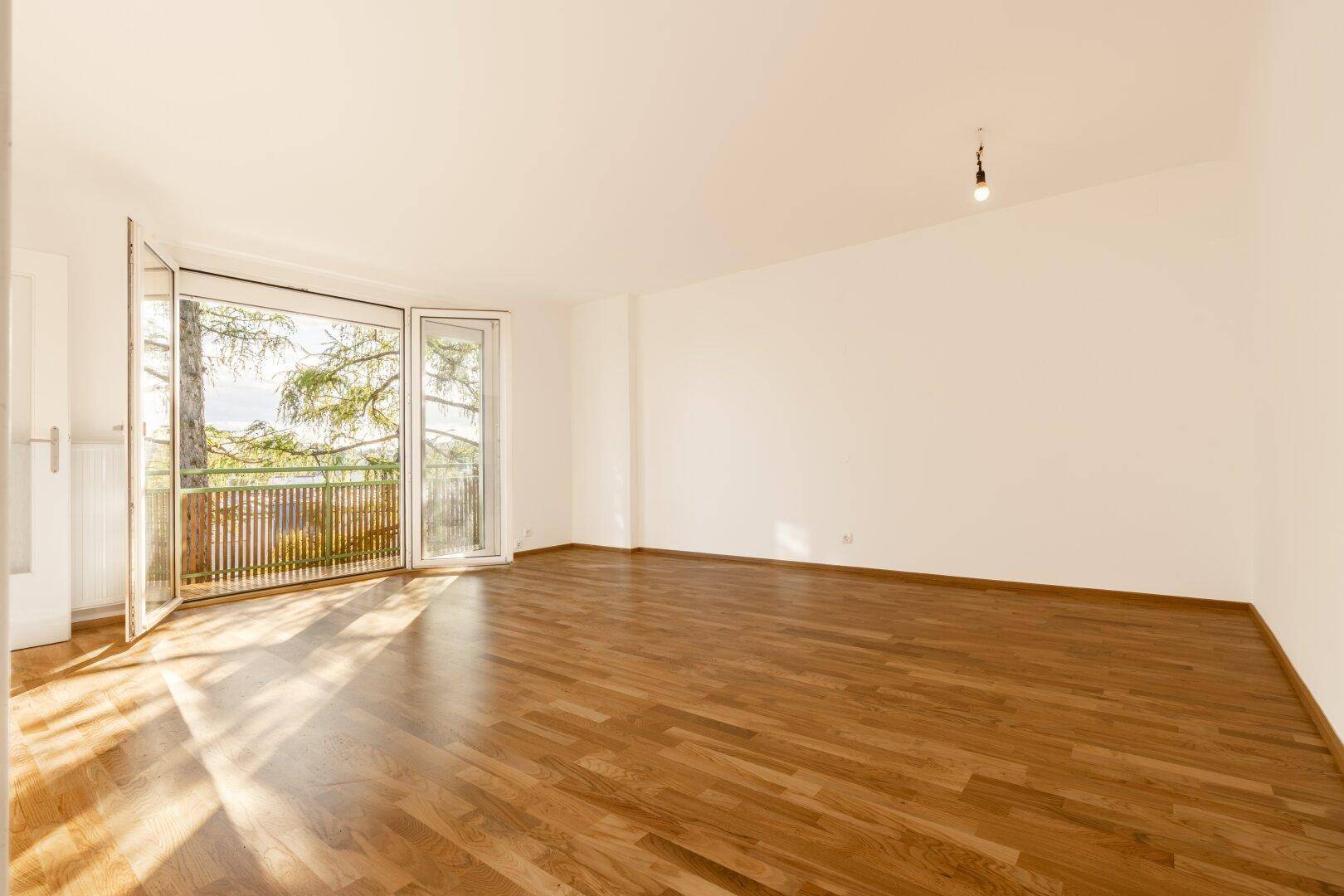 Geräumiges, helles Zimmer mit Parkettboden und großen Fenstern, die viel Sonnenlicht hereinlassen.