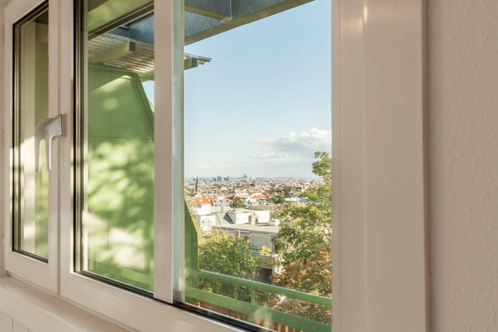 Fenster mit weitem Blick über die Stadt und die umliegende grüne Landschaft an einem sonnigen Tag.