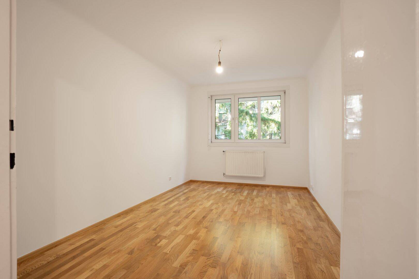 Helles Schlafzimmer mit Parkettboden und Blick ins Grüne durch das Fenster, sehr gepflegt.