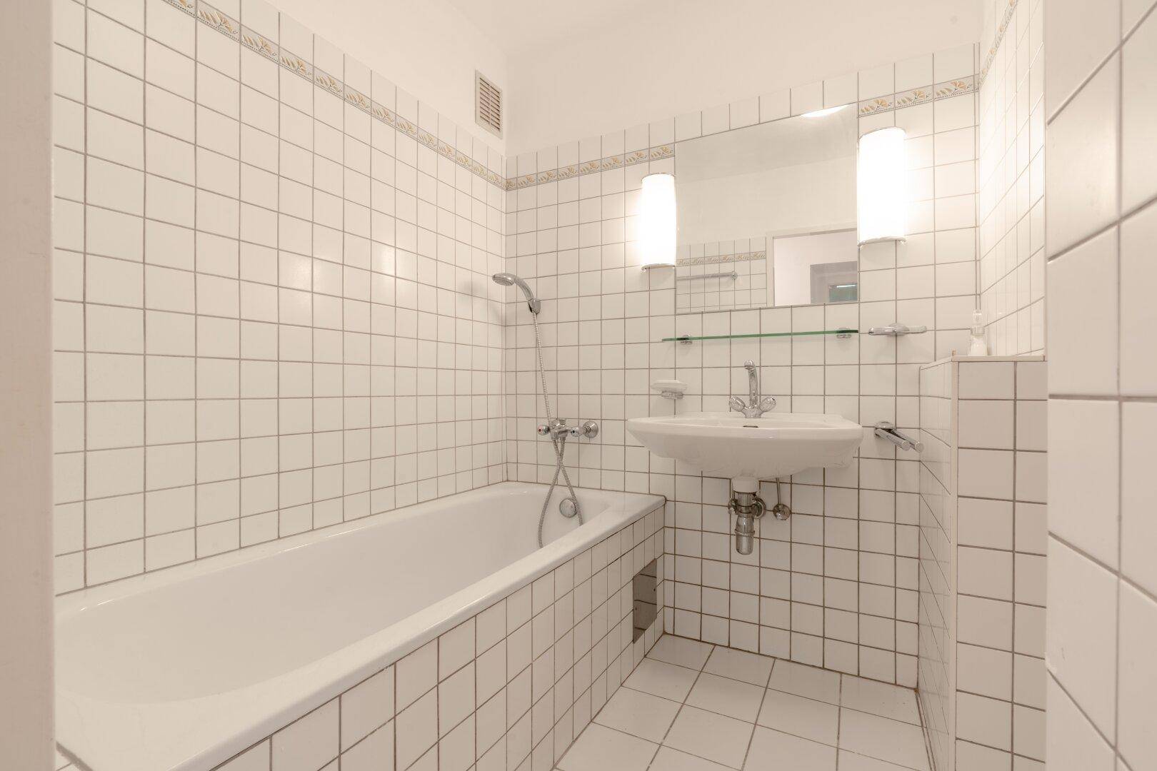 Badezimmer mit Badewanne, Waschbecken und weißen Fliesen an Wänden und Boden, sehr gepflegt.