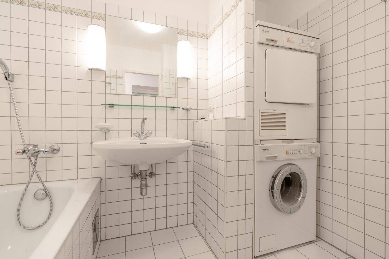 Badezimmer mit Waschmaschine, Trockner, Badewanne und weißen Fliesen, funktional und hell.