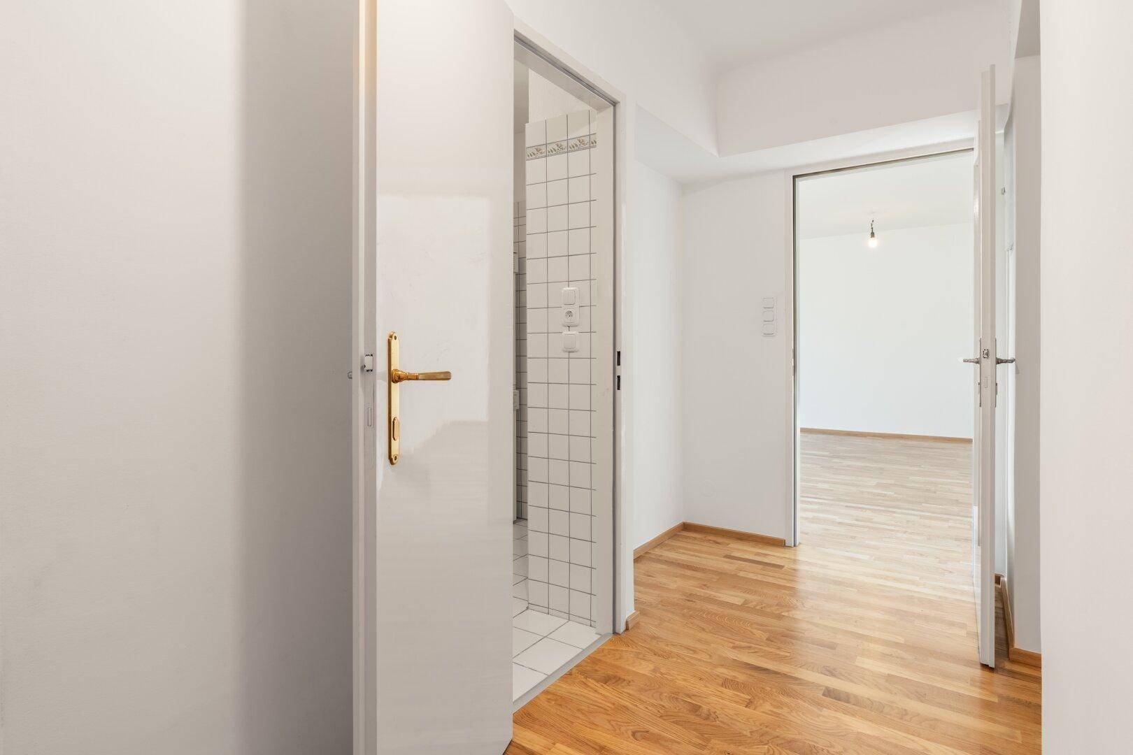 Heller Flur mit Parkettboden und Zugang zu einem Badezimmer mit Dusche, modern und sauber.