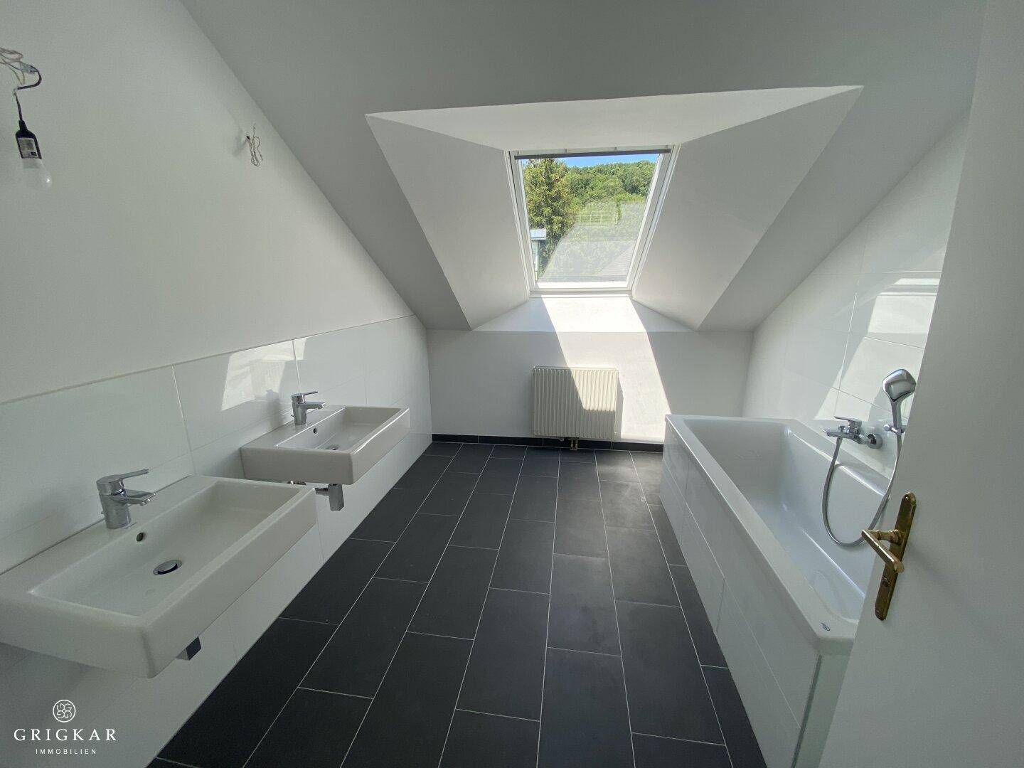 Helles Badezimmer mit zwei Waschbecken, Badewanne und Dusche unter einem großen Dachfenster.