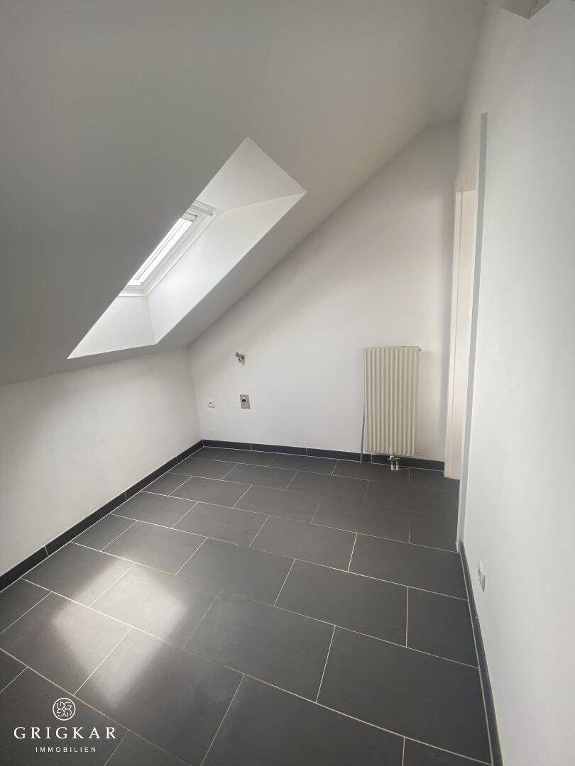 Kleiner Raum mit dunklem Fliesenboden, Dachschräge und einem Dachfenster.