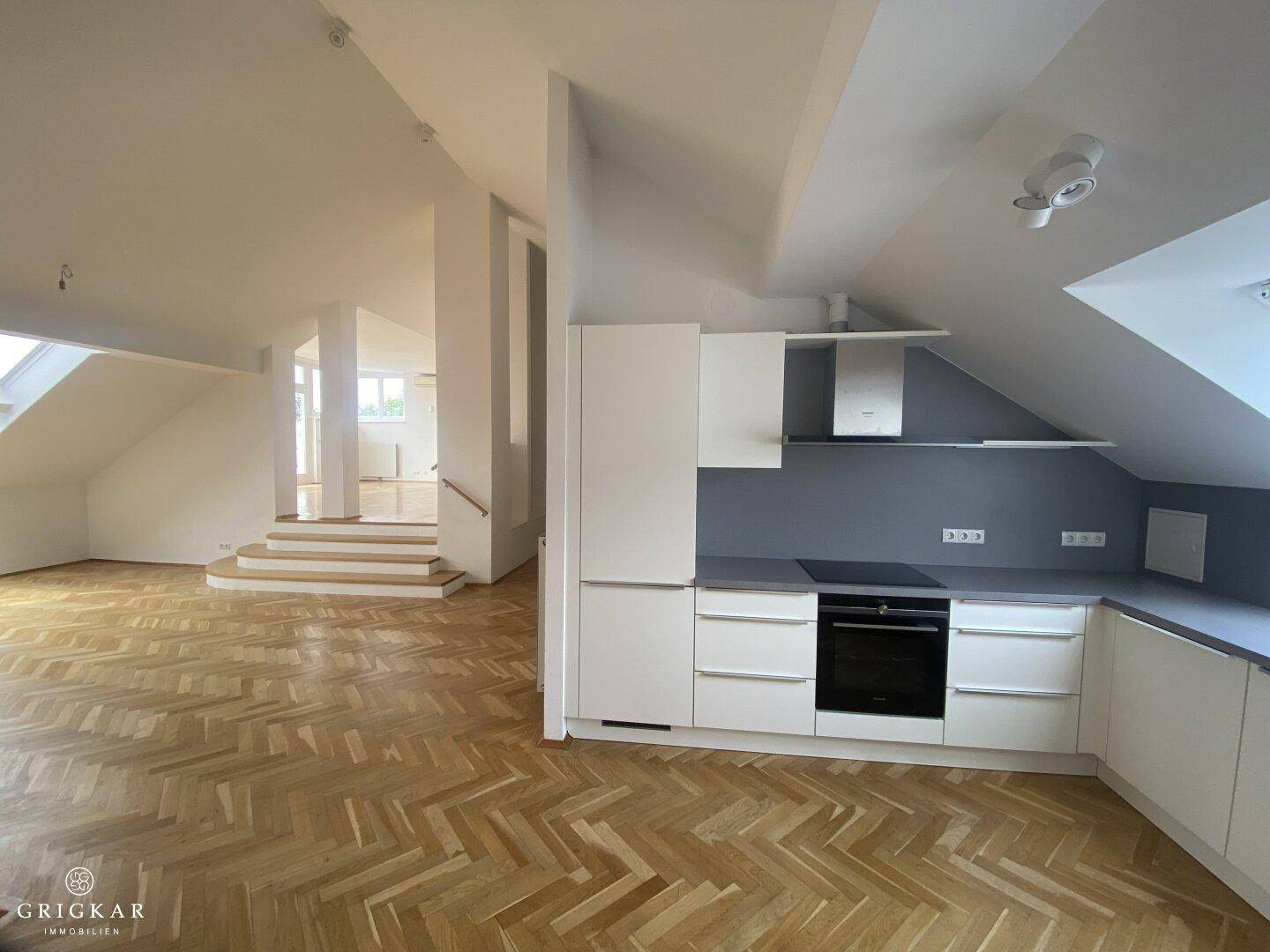 Offener Wohnbereich mit Fischgrätparkett, Dachschrägen und Blick auf die angrenzende Küche.