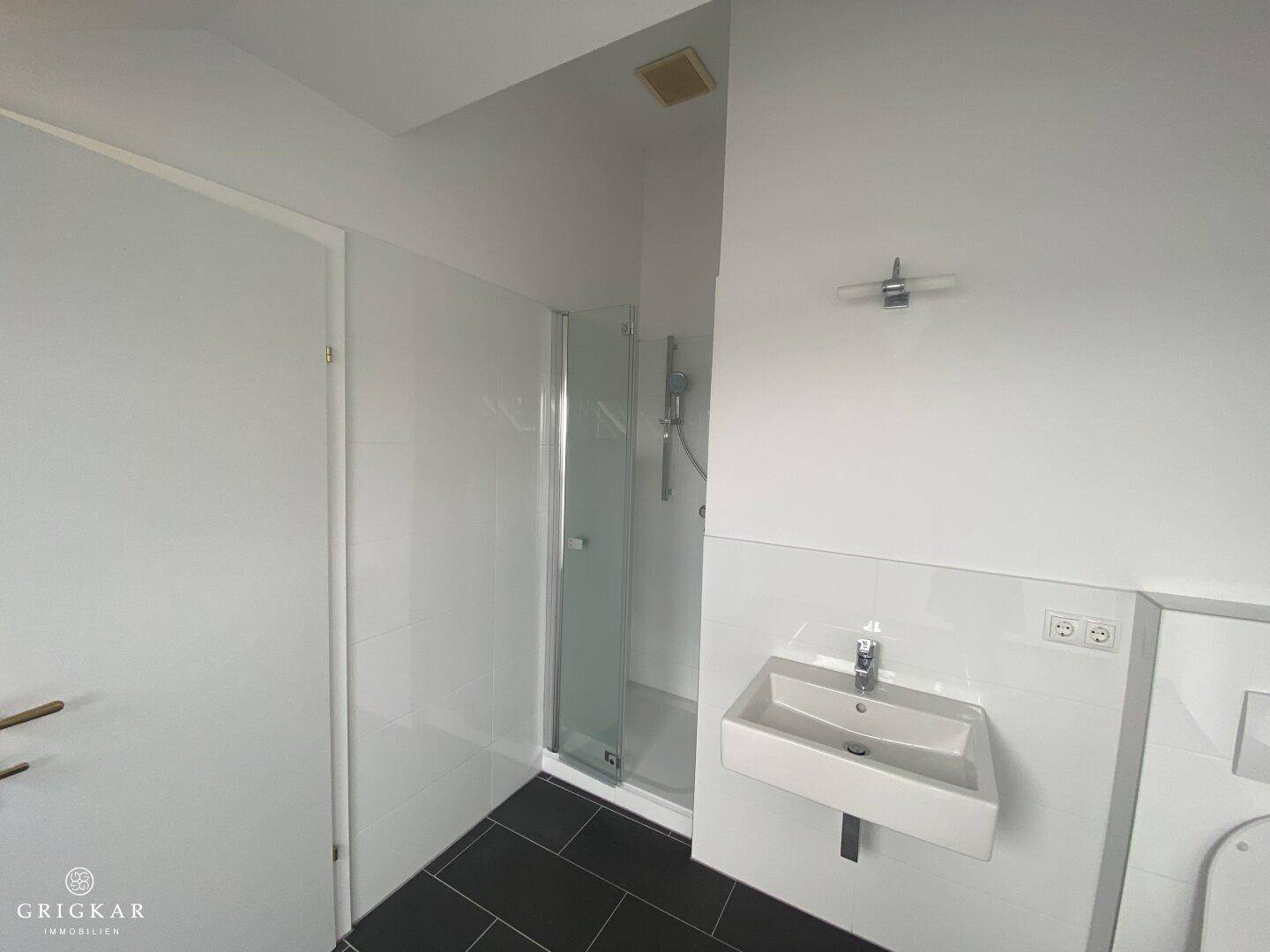 Kleines Badezimmer mit Duschkabine, Einzelwaschbecken und dunklem Fliesenboden.