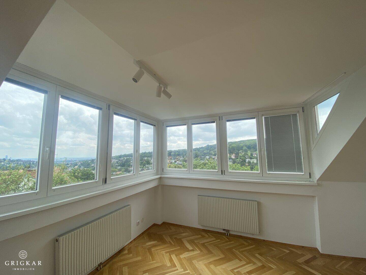 Heller Raum mit großen Fenstern, die einen weiten Blick ins Grüne und auf die Stadt bieten.
