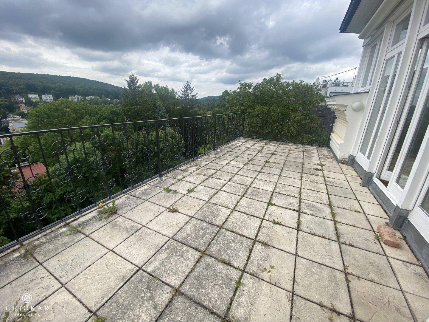 Große Terrasse mit älteren Fliesen und schmiedeeisernem Geländer unter bewölktem Himmel.