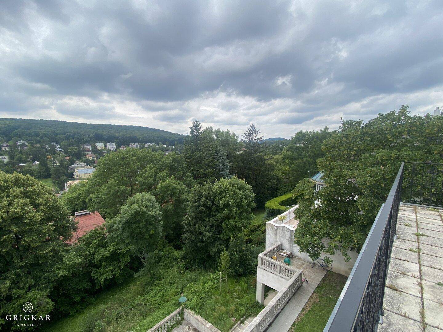 Weitläufiger Blick von einer gefliesten Terrasse über grüne Hügel und eine Stadtlandschaft unter bewölktem Himmel.