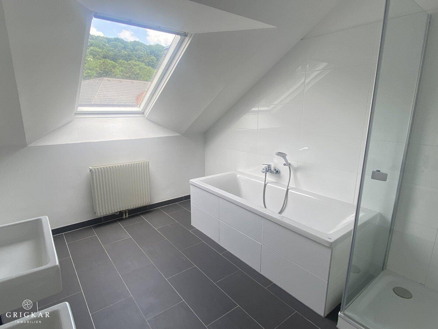 Modernes Badezimmer mit dunklen Fliesen, Badewanne, Dusche und großem Dachfenster.