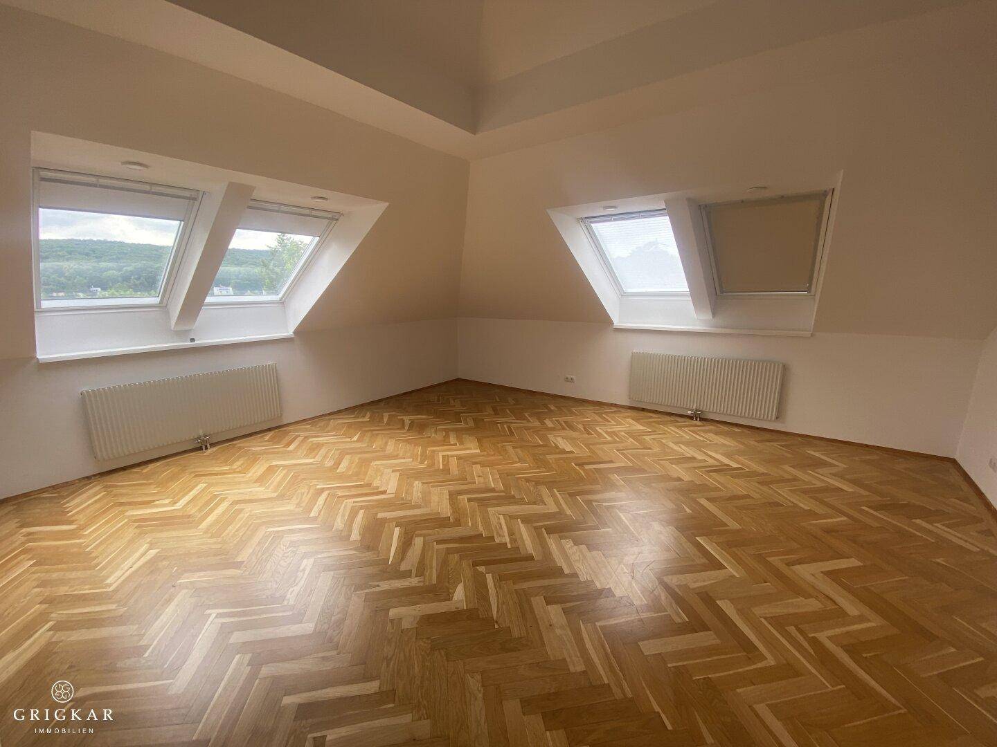 Helles Dachzimmer mit Fischgrätparkett, Dachschrägen und zwei Dachfenstern für viel Licht.