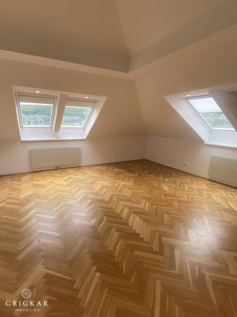 Gemütliches Zimmer im Dachgeschoss mit Fischgrätparkett, Dachschrägen und zwei Dachfenstern.