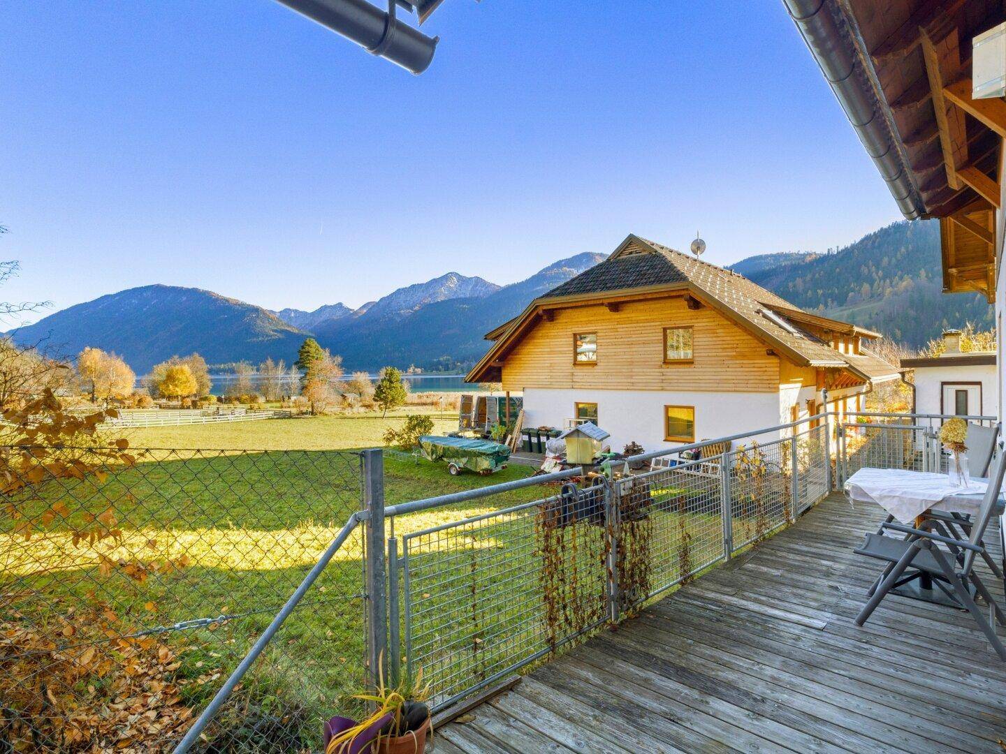 Holzbalkon mit Metallgeländer und weitem Blick über grüne Wiesen zum See.