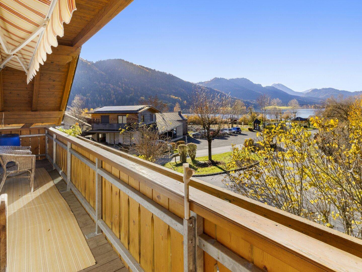 Geräumiger Holzbalkon mit Markise und Panoramablick auf den See und die Berge.