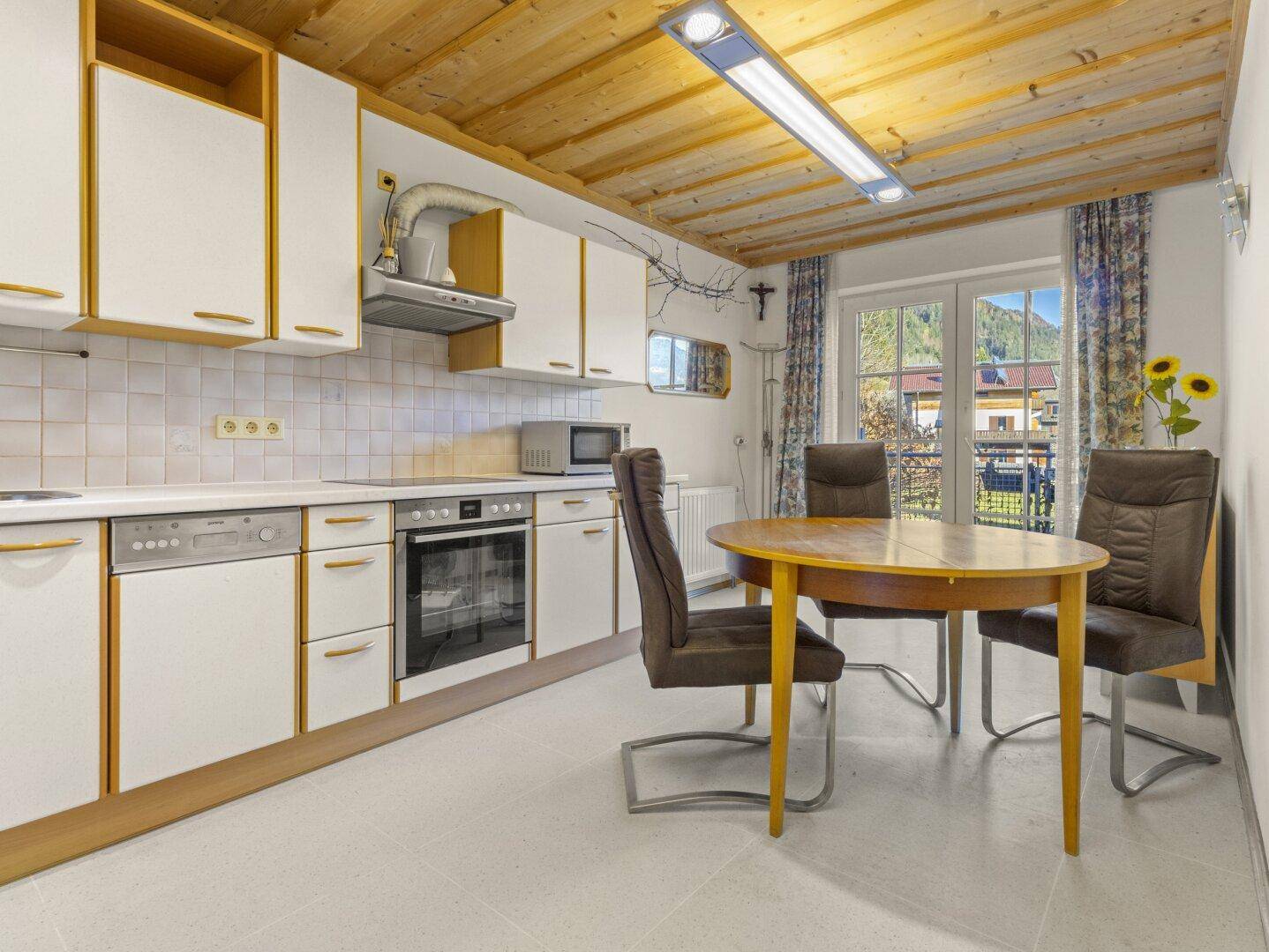 Helle Wohnküche mit weißen Schränken, Essbereich und Holzbalkendecke.