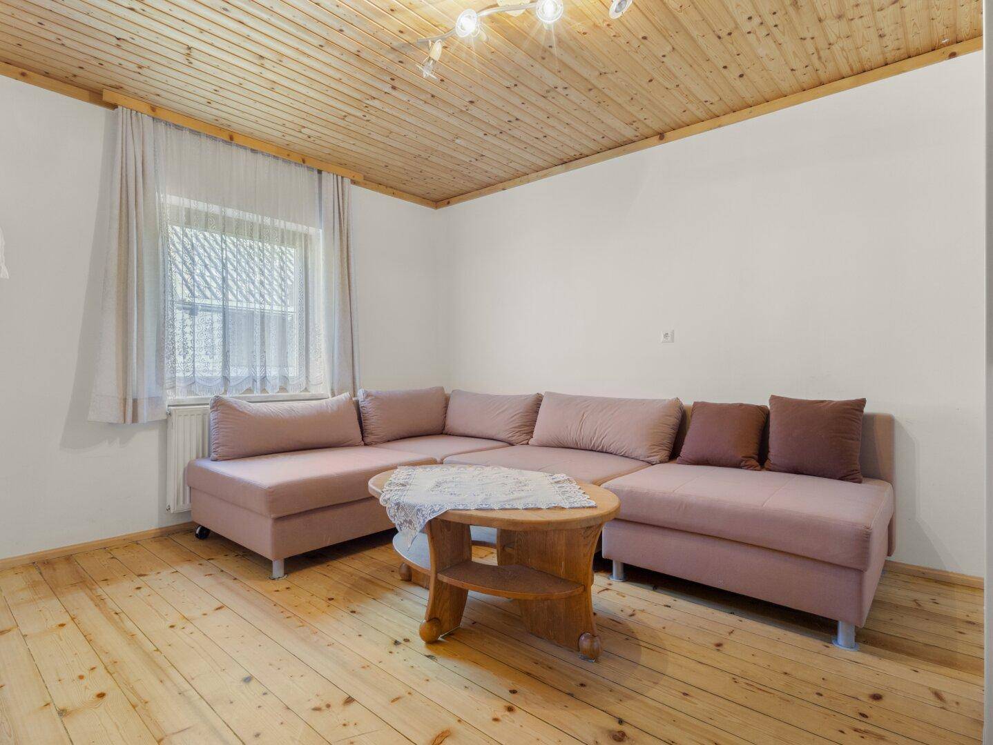 Gemütliches Wohnzimmer mit großem Ecksofa, Holzboden und Holzpaneeldecke.