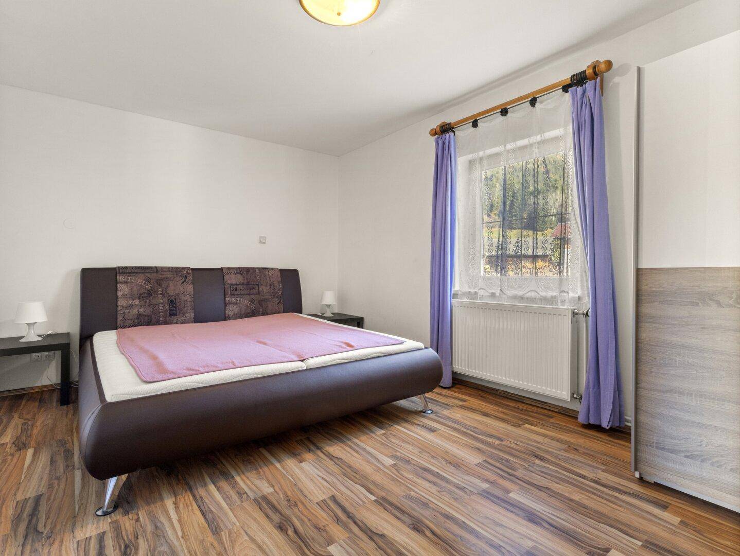 Schlafzimmer mit Doppelbett, Kleiderschrank und Fenster mit Blick ins Grüne.