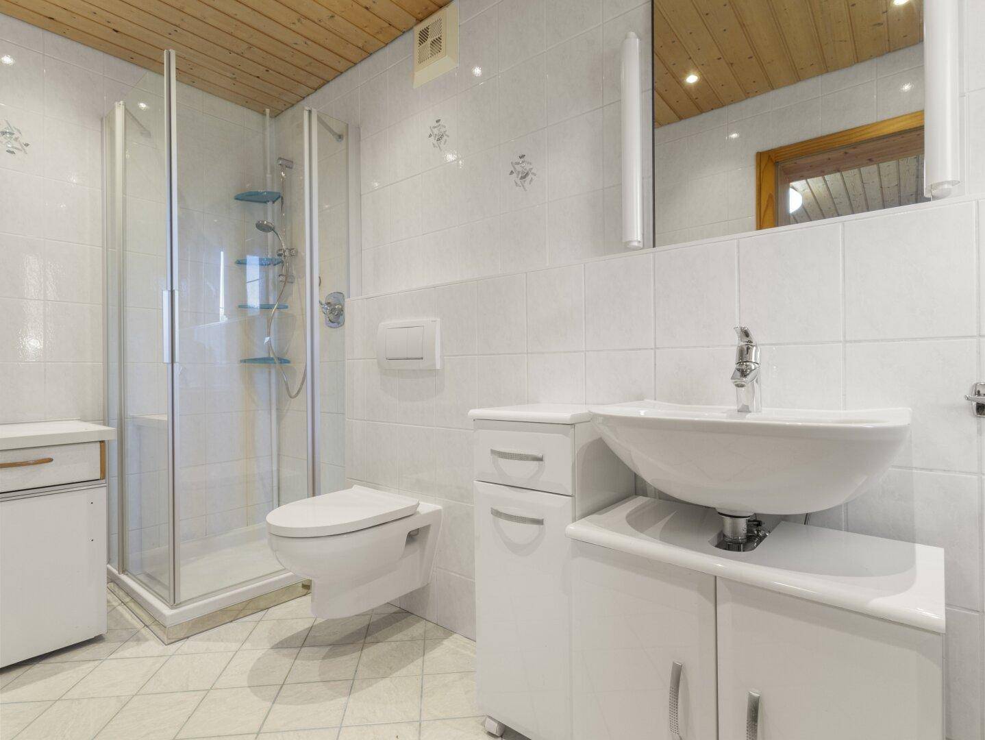 Helles Badezimmer mit Duschkabine, WC, Waschtisch und Holzpaneeldecke.