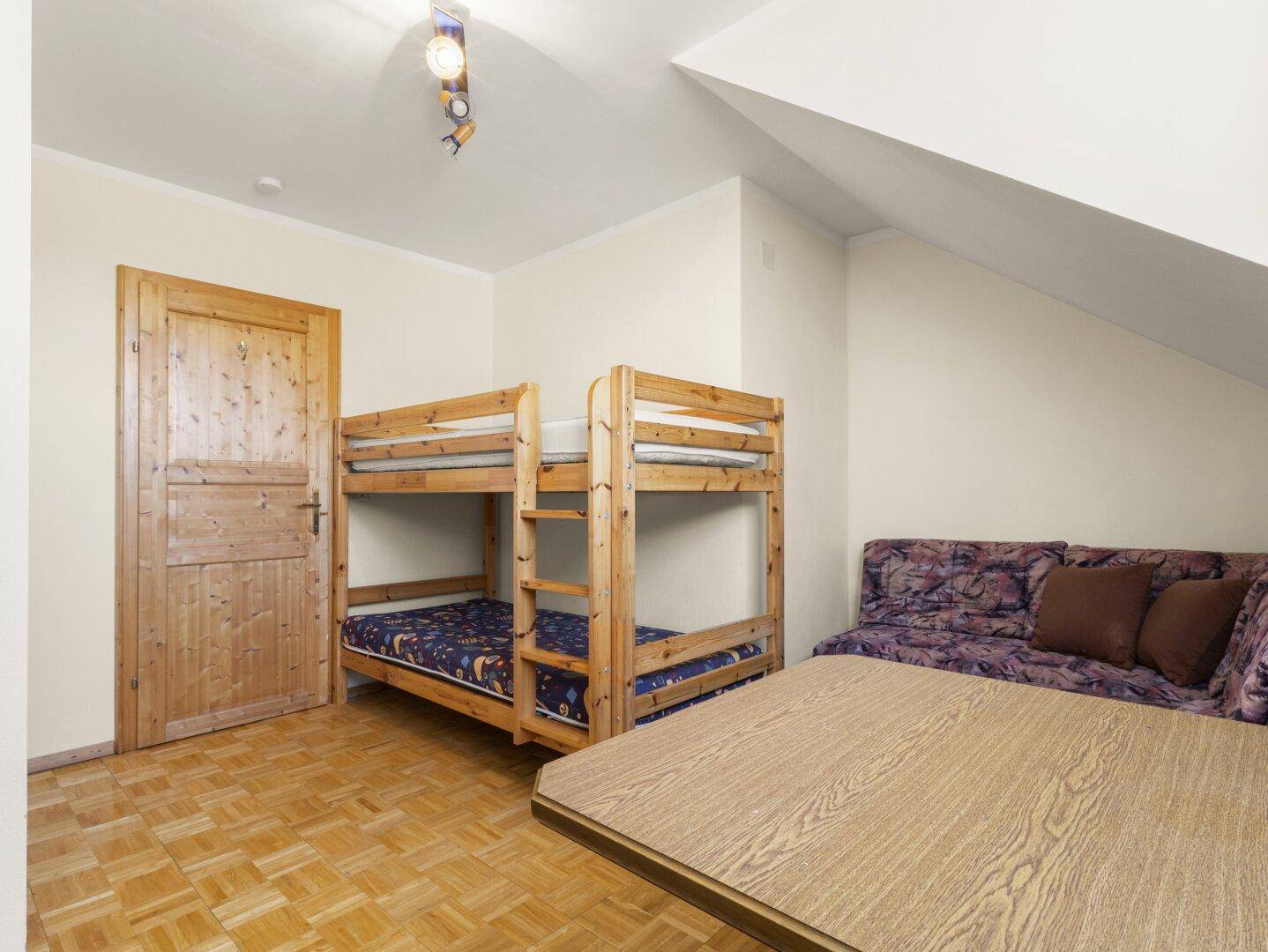 Schlafzimmer mit Etagenbetten, Sofa und Holzboden unter einer Dachschräge.