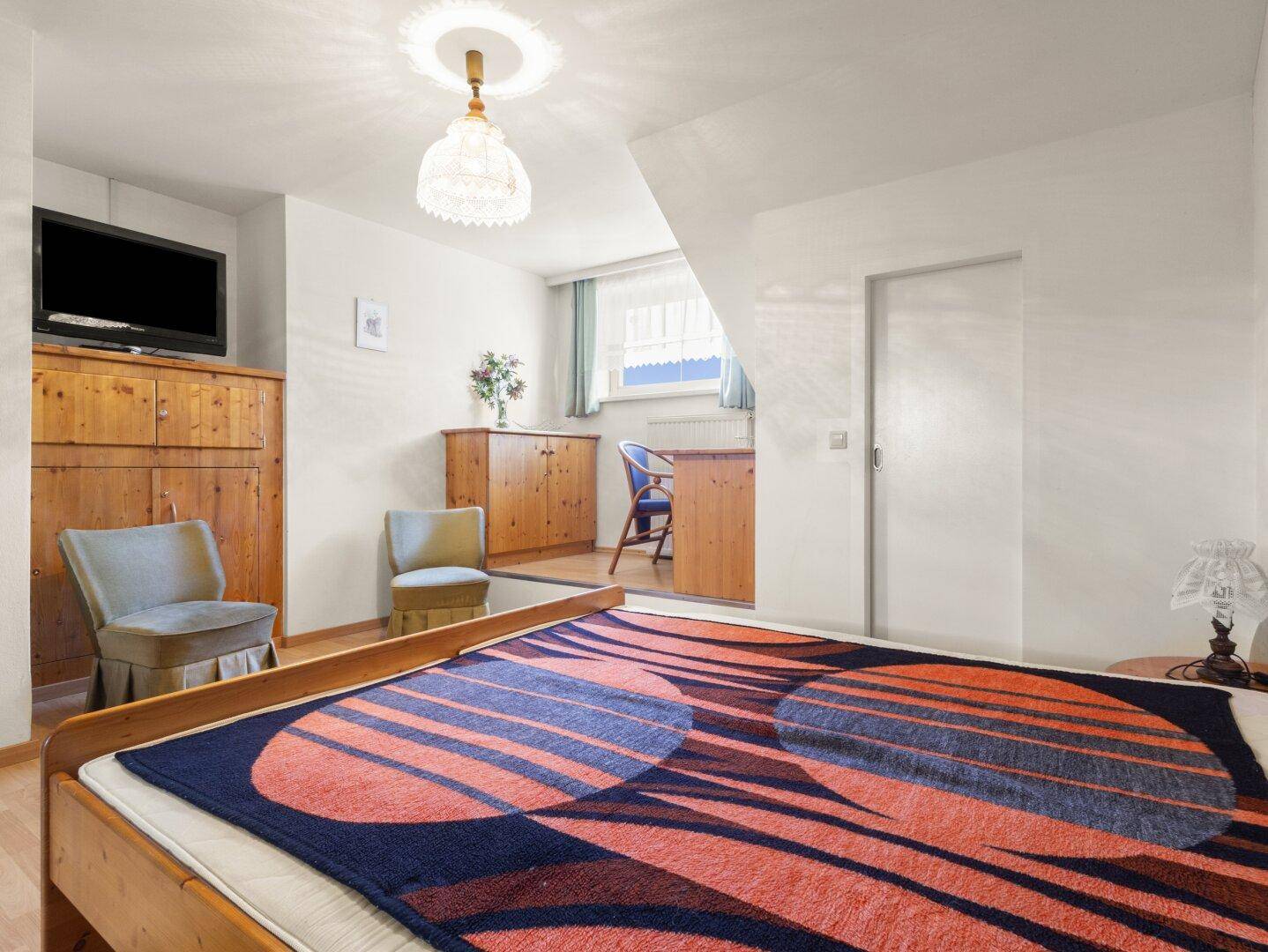 Gemütliches Schlafzimmer mit Holzelementen, Dachschräge und einem kleinen Arbeitsbereich.