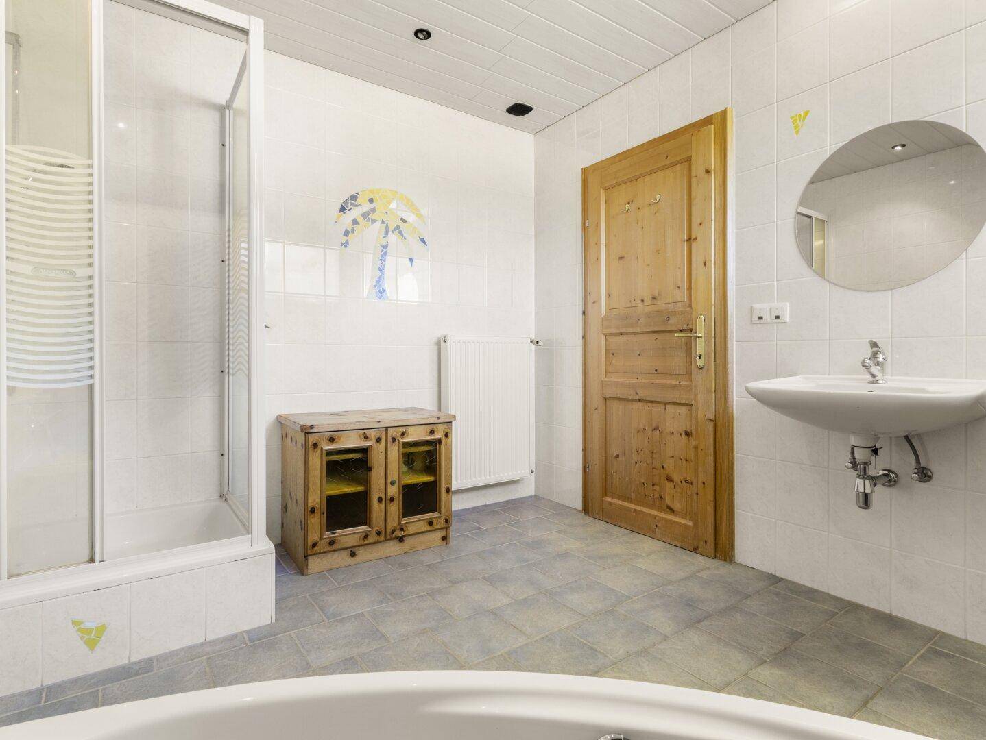 Helles Badezimmer mit Dusche, Waschbecken und Holzmöbeln, ausgestattet mit weißen Fliesen.