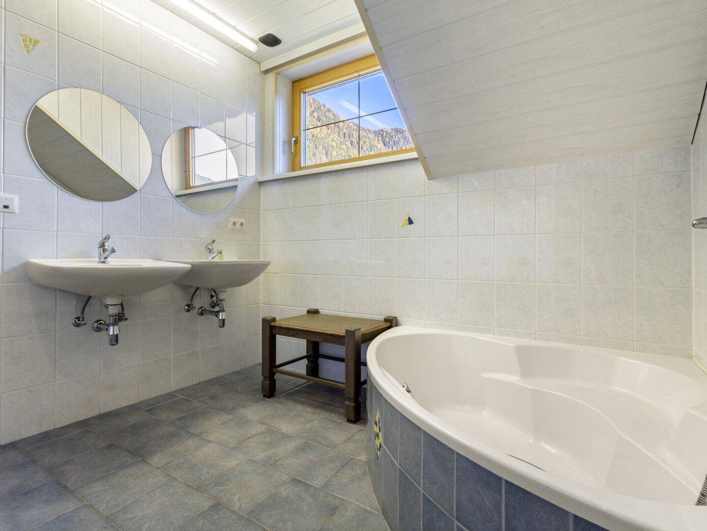 Geräumiges Badezimmer mit zwei Waschbecken, Badewanne und Bergblick durch das Fenster.
