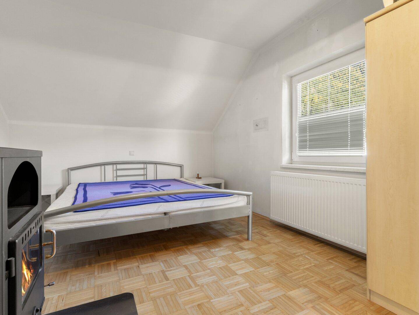 Helles Schlafzimmer mit Holzboden, Dachschräge und einem gemütlichen Holzofen.