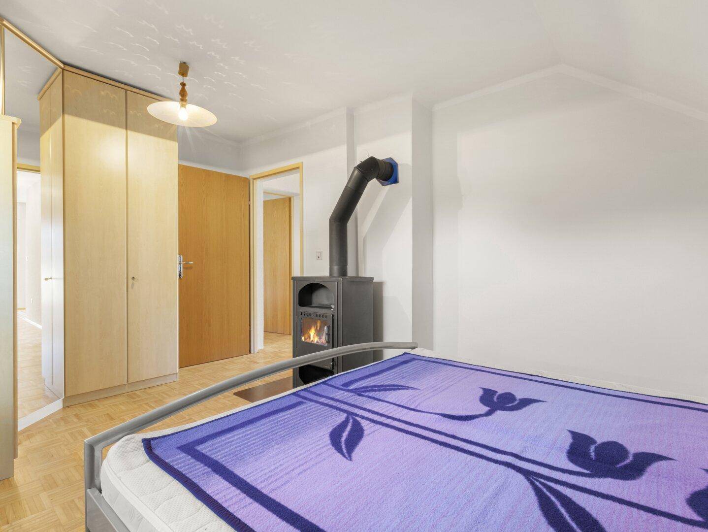 Schlafzimmer mit Holzboden, Einbauschränken und einem modernen Holzofen als Wärmequelle.