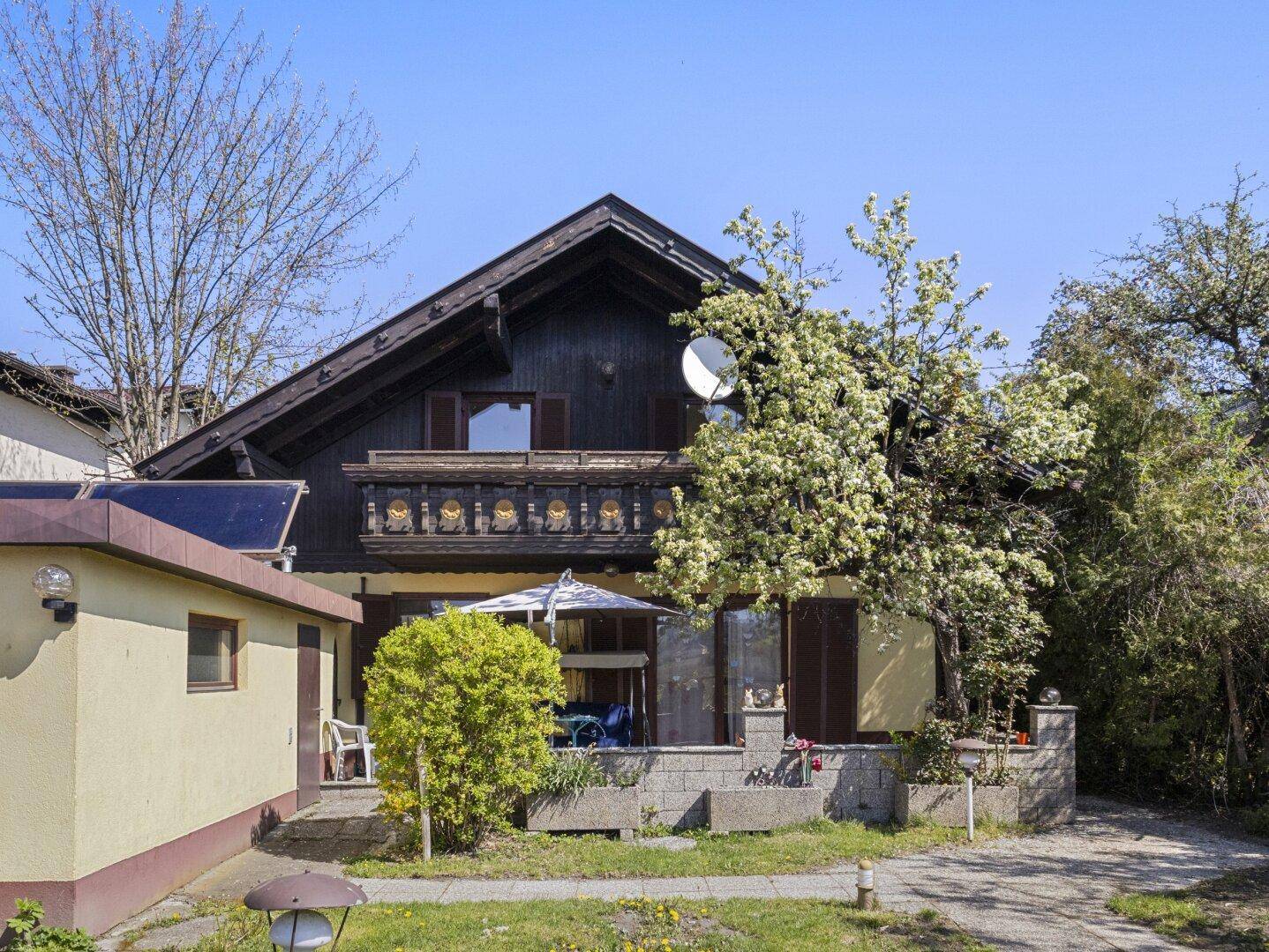Vorderansicht des Hauses mit traditionellem Holzbalkon, Terrasse und gepflegtem Vorgarten.