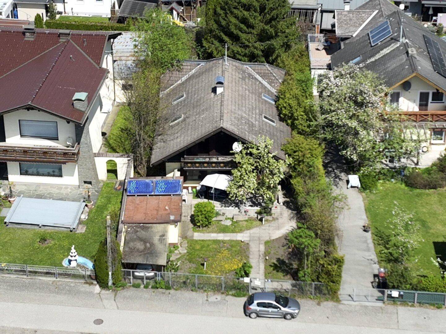Luftaufnahme des Hauses mit Garten, Carport und umliegender Wohnbebauung unter blauem Himmel.