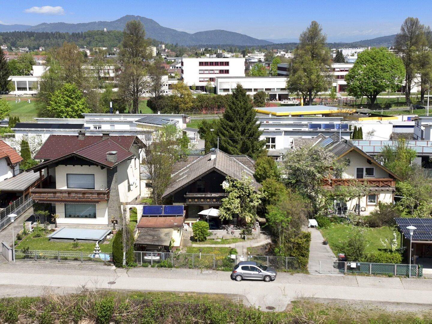 Weitläufige Luftaufnahme der Wohngegend mit dem Haus, umgeben von Grünflächen und Bergen im Hintergrund.