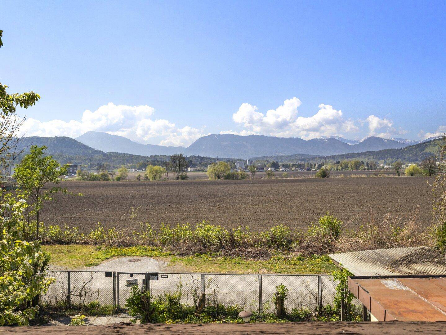 Panoramablick über weite Felder und die beeindruckende Bergkette unter einem klaren blauen Himmel.
