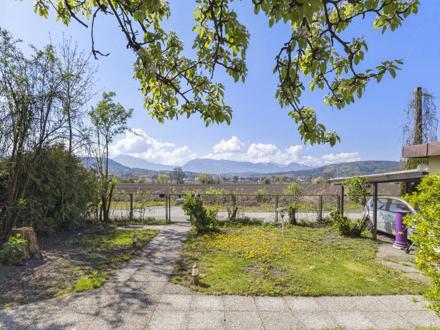 Vorgarten mit Rasenfläche, gepflastertem Weg und weitem Blick auf die umliegende Landschaft und Berge.
