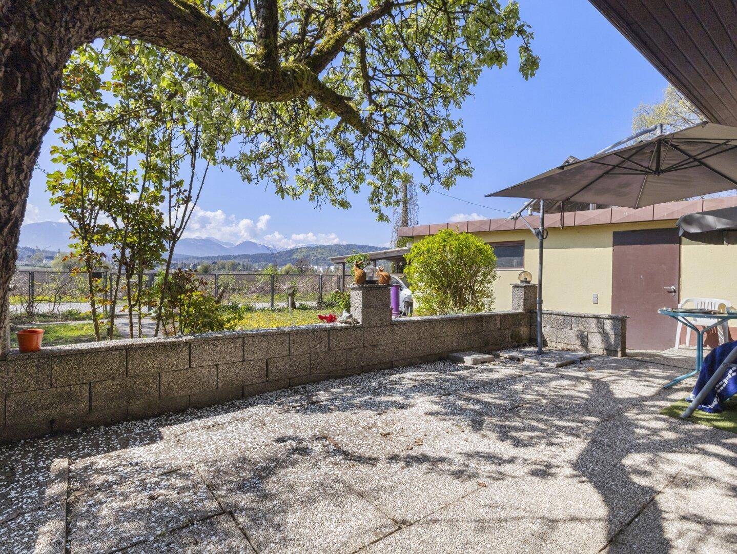 Sonniger Terrassenbereich mit Steinmauer, Sonnenschirm und weitem Blick auf die Landschaft und Berge.