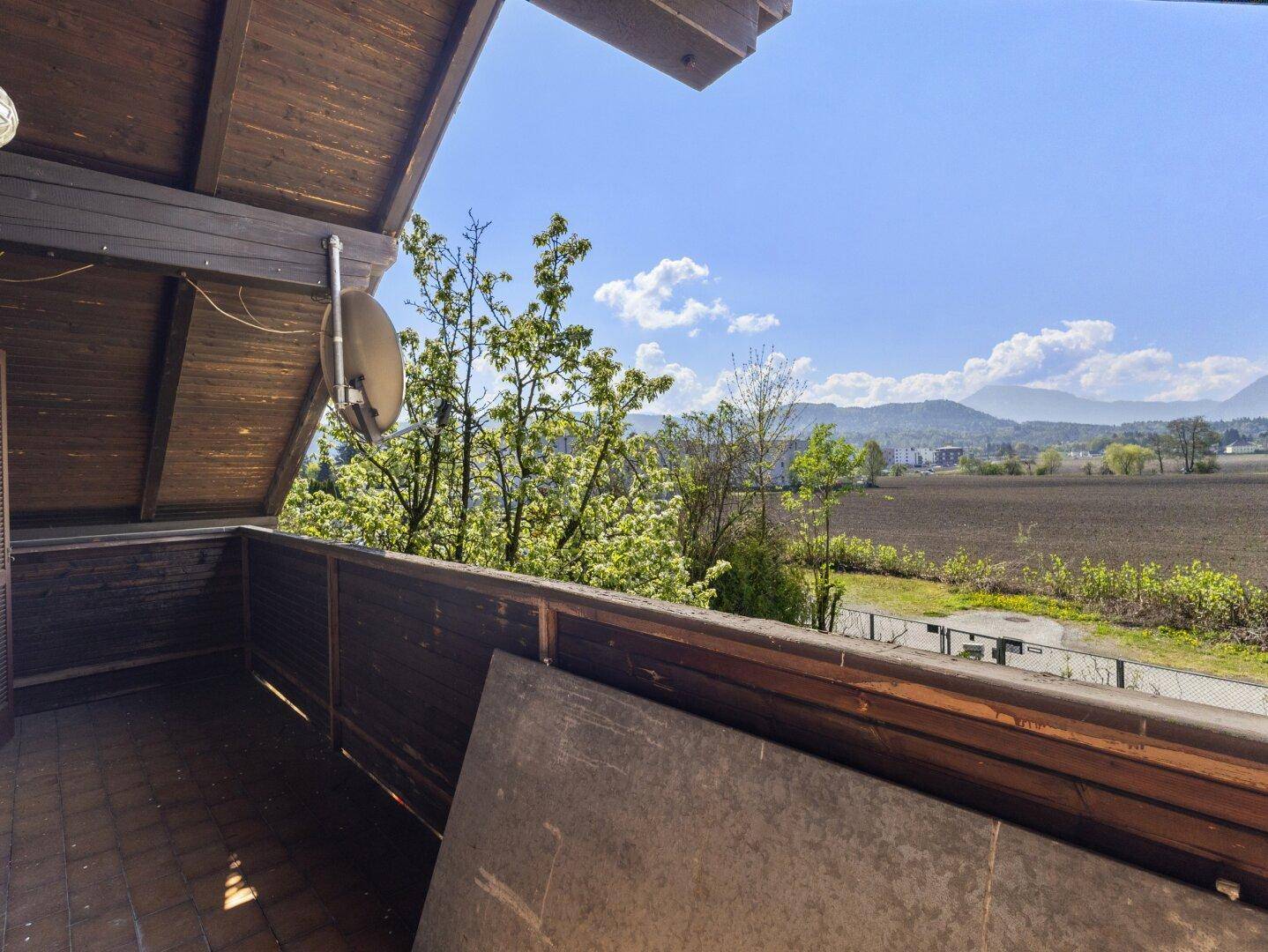 Balkon mit Holzboden und Geländer, bietet einen weiten Blick über Felder und die Berglandschaft.