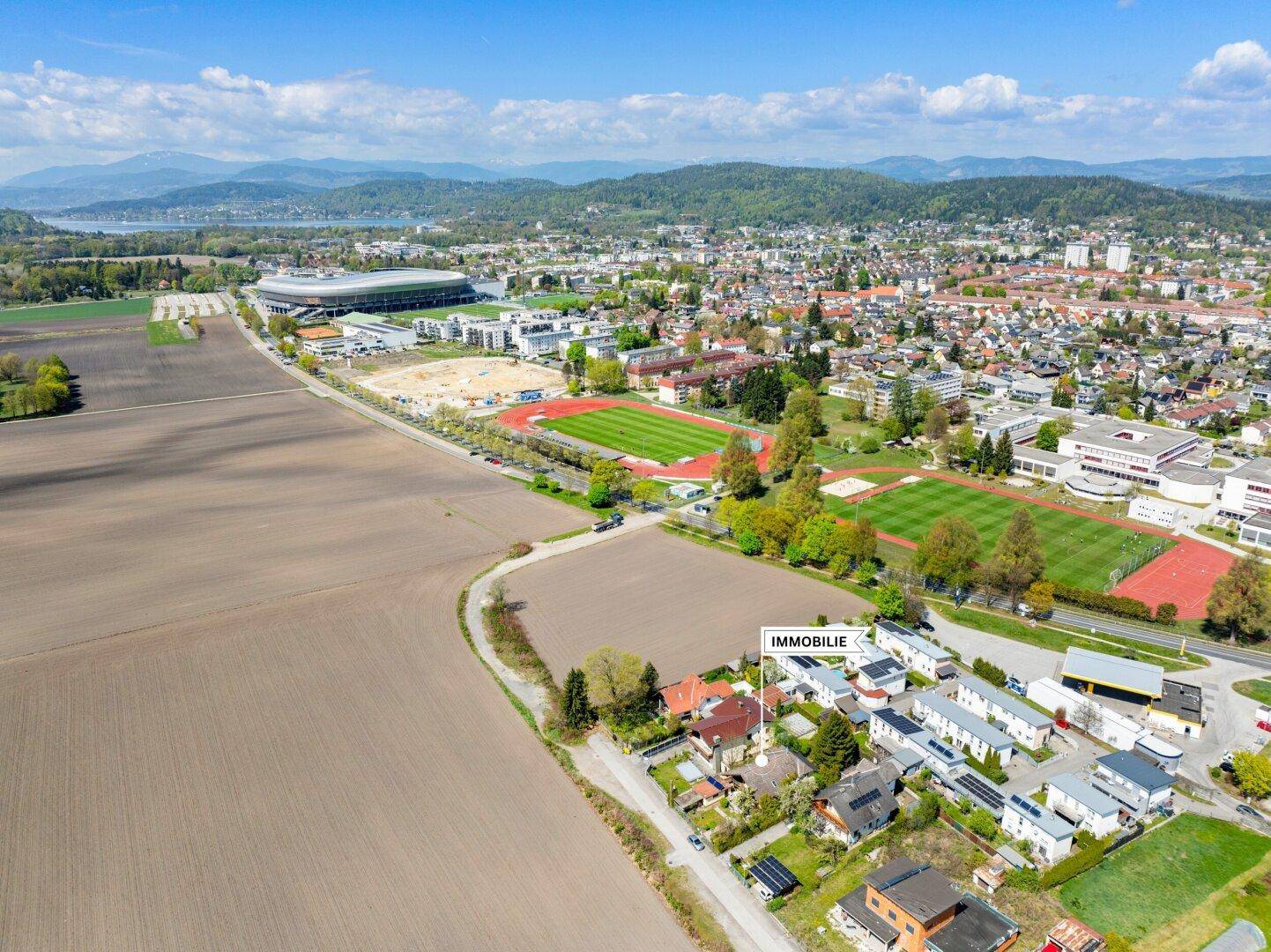 Weitläufige Luftaufnahme der Stadt und Umgebung, mit der Immobilie nahe Sportanlagen und einem See.
