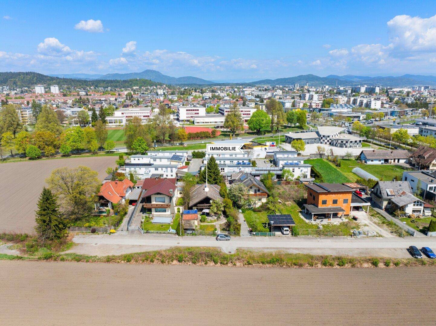 Luftaufnahme der Immobilie in einer Wohnsiedlung, umgeben von Feldern und mit Bergblick im Hintergrund.