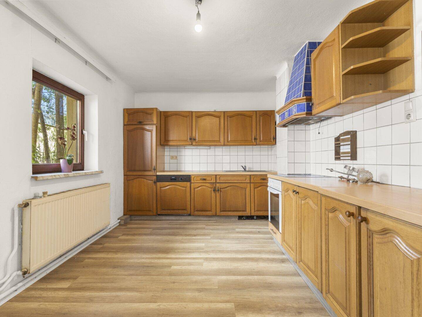 Geräumige Küche im traditionellen Stil mit Holzschränken, weißen Fliesen und Fensterblick ins Grüne.