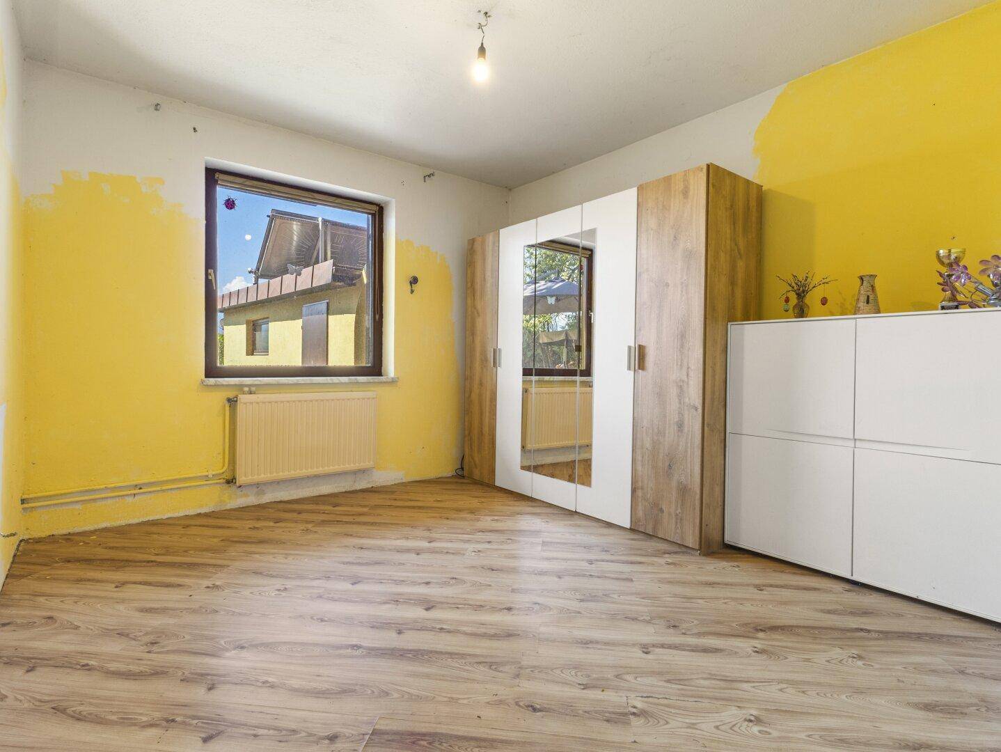 Schlafzimmer mit gelb gestrichenen Wänden, Laminatboden und einem modernen Kleiderschrank.
