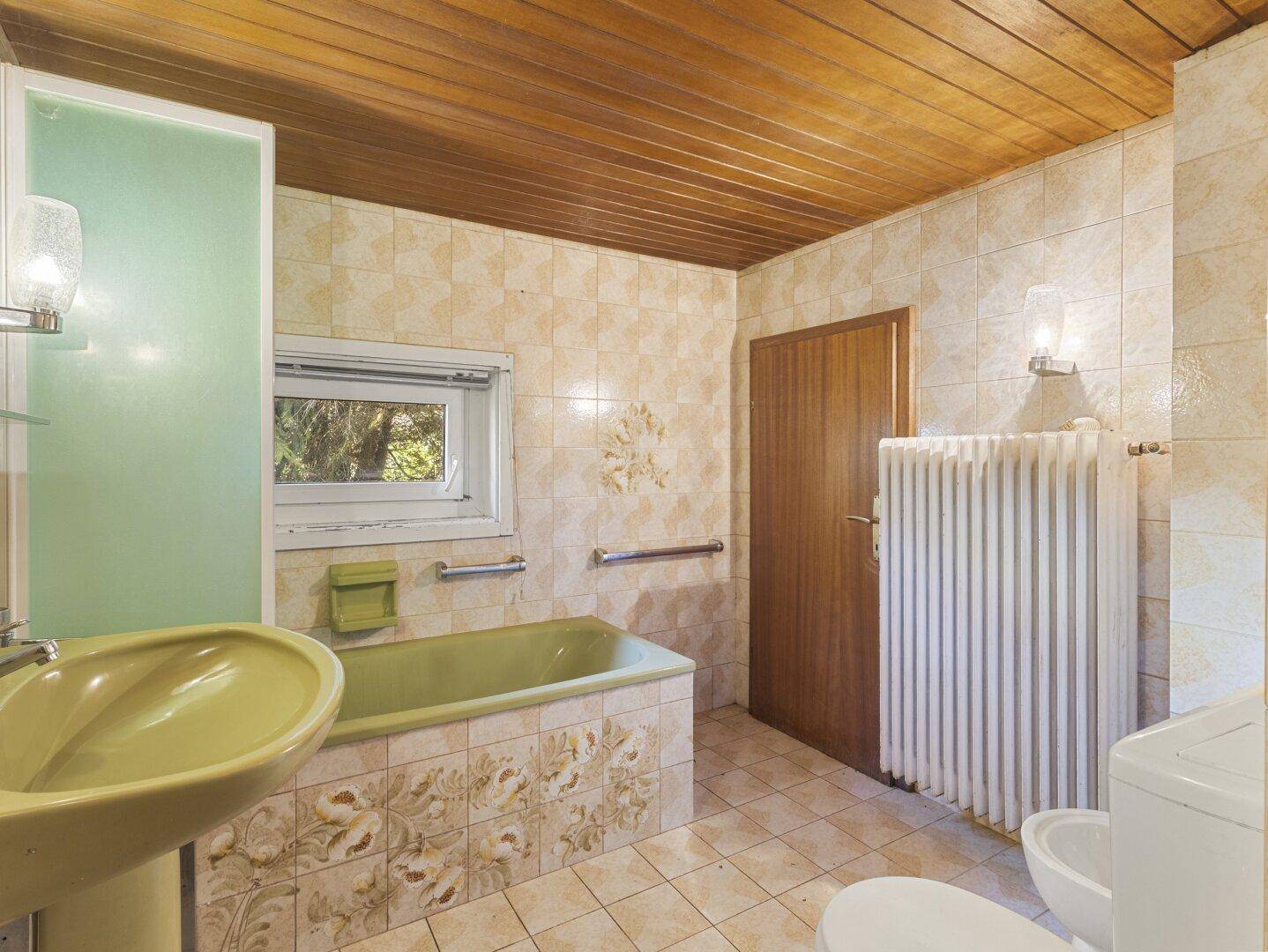Badezimmer im 80er-Jahre-Stil mit beigefarbenen Fliesen, grüner Badewanne und Fenster.