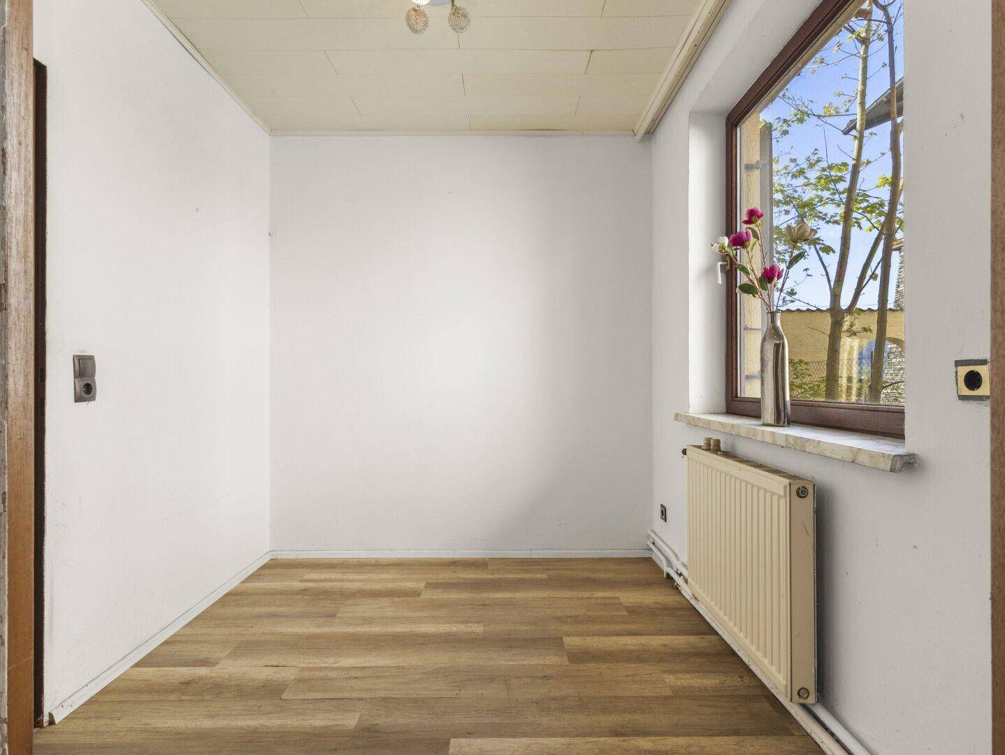 Heller Flur oder kleiner Raum mit Laminatboden und einem Fenster, das Tageslicht hereinlässt.