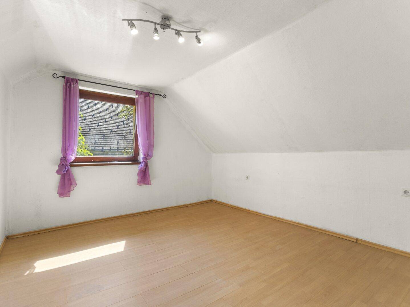 Helles Schlafzimmer im Dachgeschoss mit Laminatboden, schrägen Wänden und einem Fenster.