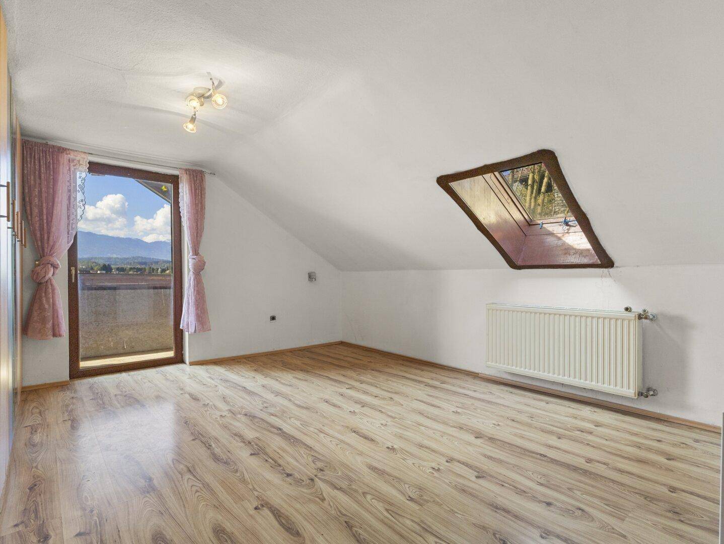 Schlafzimmer im Dachgeschoss mit Laminatboden, Dachfenster und Zugang zu einem Balkon mit Bergblick.