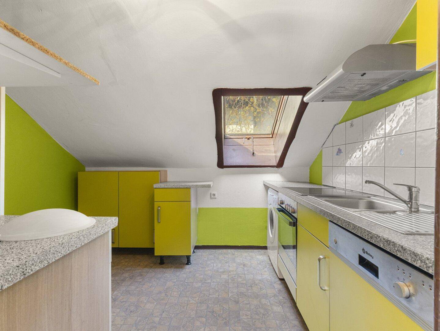 Dachgeschossküche mit gelb-grünen Schränken, Granitarbeitsplatte und Dachfenster.