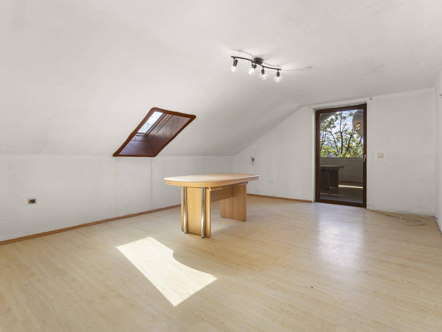 Geräumiger Raum im Dachgeschoss mit Laminatboden, Dachfenster und Zugang zu einem Balkon.