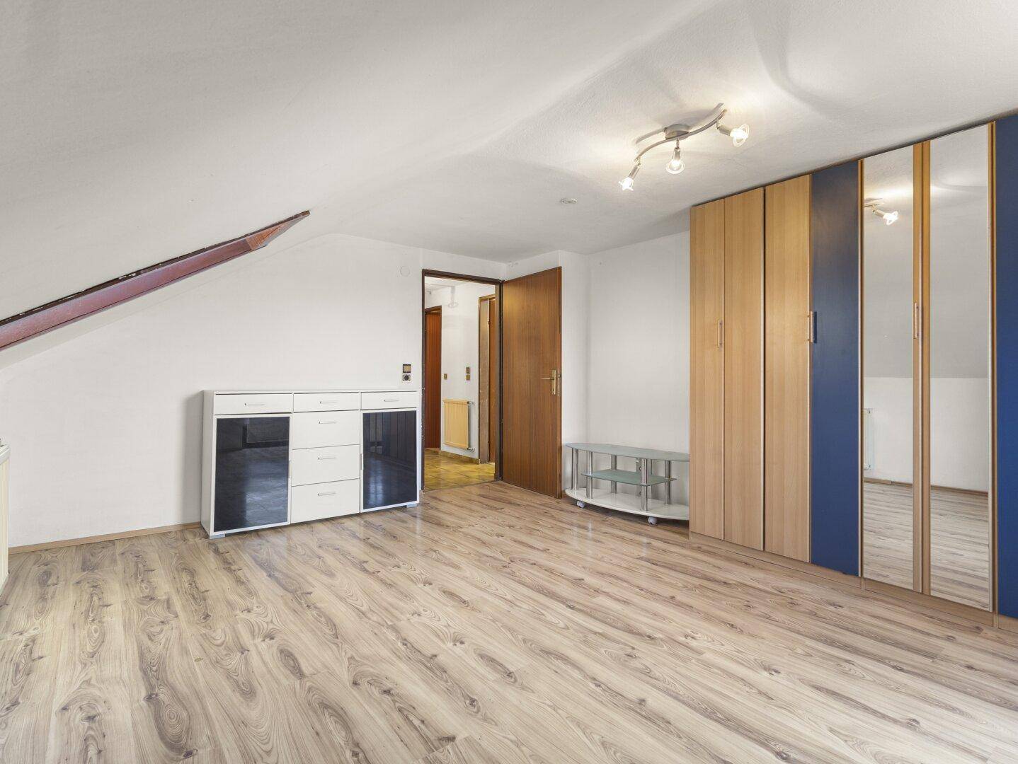 Schlafzimmer im Dachgeschoss mit Laminatboden, Schränken und Zugang zu einem weiteren Raum.